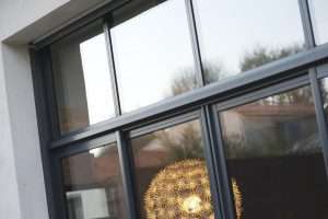 Ventanas Retalux, ventanas de PVC y aluminio en Madrid, Primer plano de una elegante ventana con marco de metal negro, Ventanas de Aluminio K-Line, con árboles y una lámpara esférica decorativa reflejada en el vidrio.
